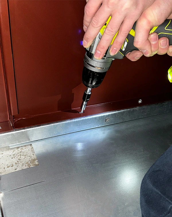 Technicien perçant la base d'un abri-bac lors d'une intervention de maintenance